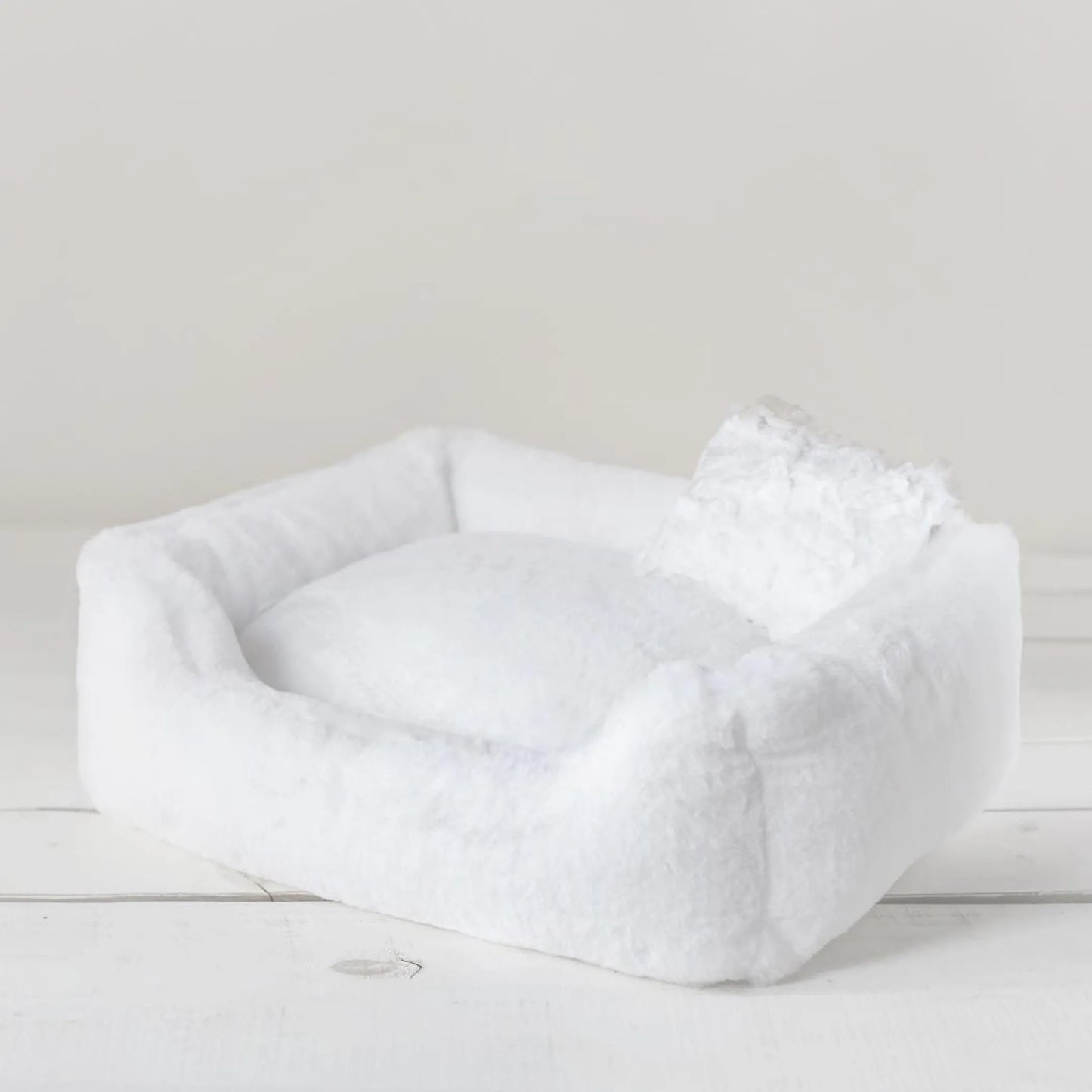 White pet bed on a light wooden floor with a neutral background