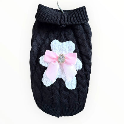 Black knitted dog sweater with a pink bow and white lace detail on a white background