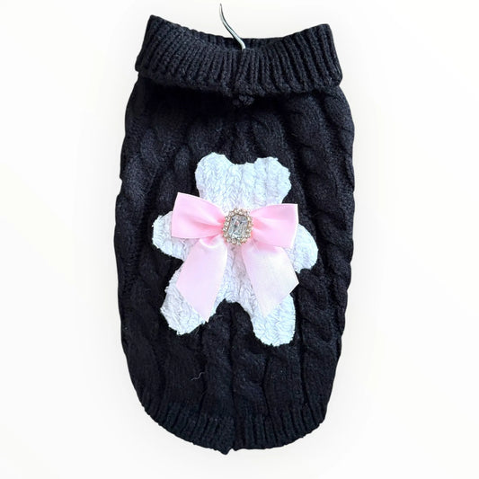 Black knitted dog sweater with a pink bow and white lace detail on a white background