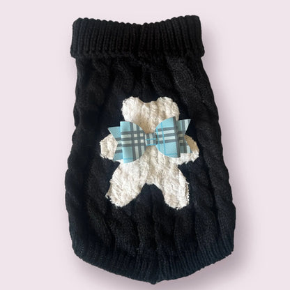 Black knitted dog sweater with white bear design and blue plaid bow on a light gray background