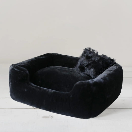 Black pet bed with a dog lying inside on a light wooden floor.