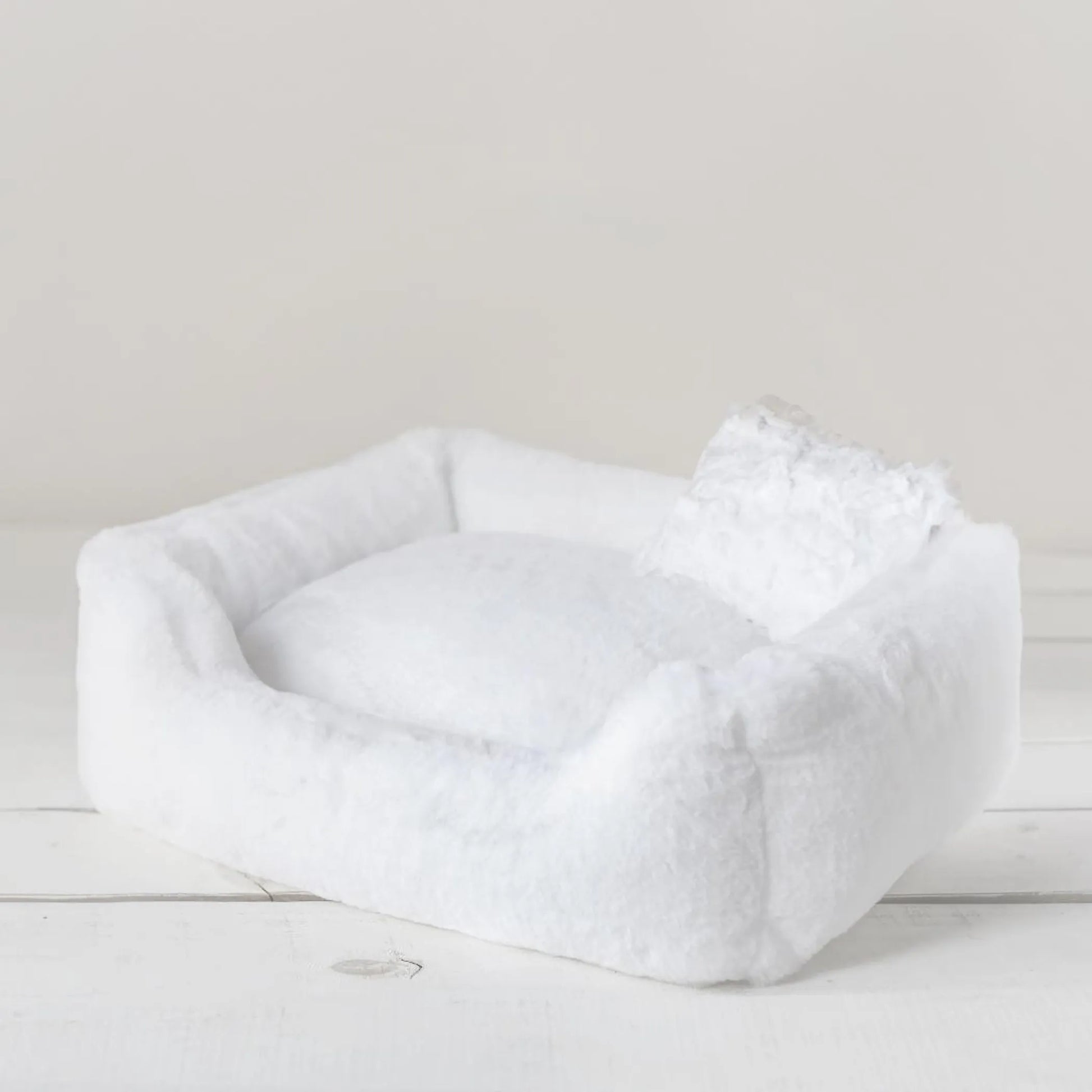 White pet bed on a light wooden floor with a neutral background